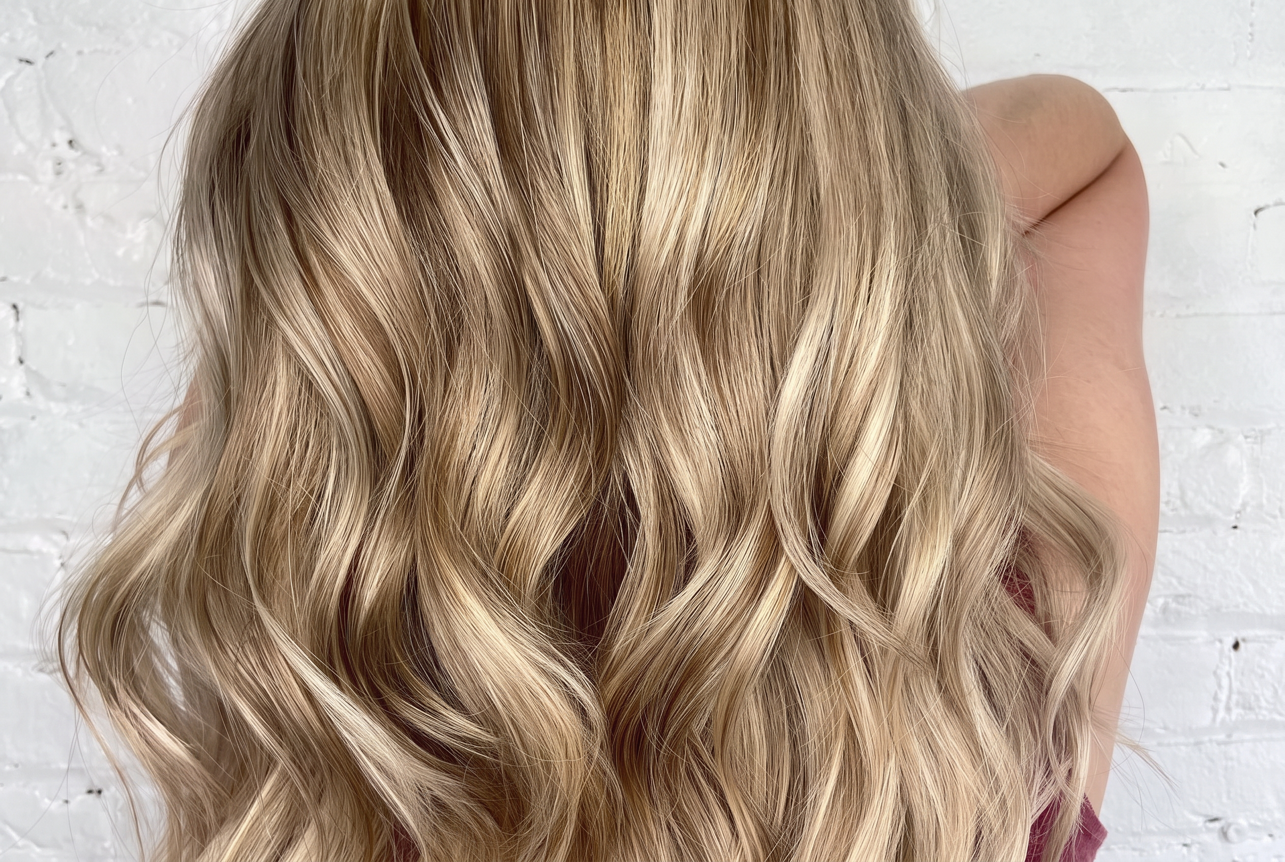 Dimensional golden beige blonde waves against a white brick wall, colour by Laila Grigley.